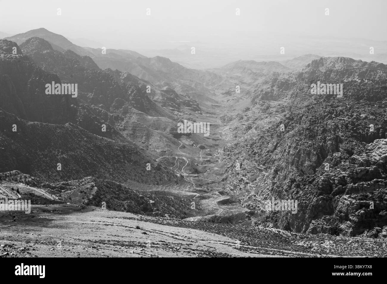 A mountain range with a valley in between. The valley is rocky and barren. The sky is cloudy and grey Stock Photo