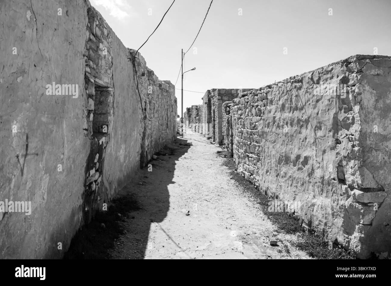 A narrow alleyway with a wire overhead. The alleyway is empty and the sky is clear Stock Photo