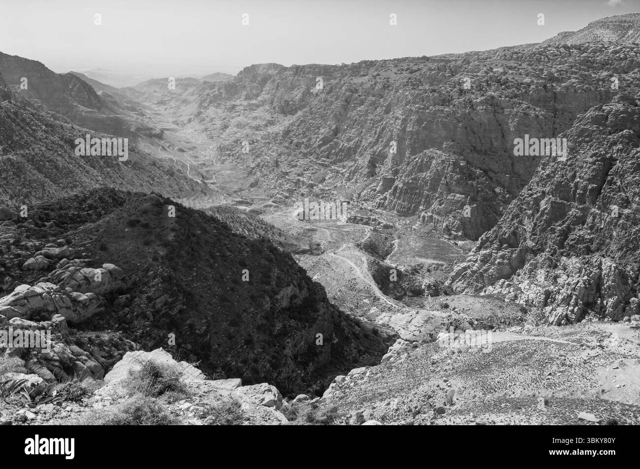 A black and white photo of a mountain range with a valley in between. The mountains are rocky and the valley is barren. Scene is one of solitude and i Stock Photo