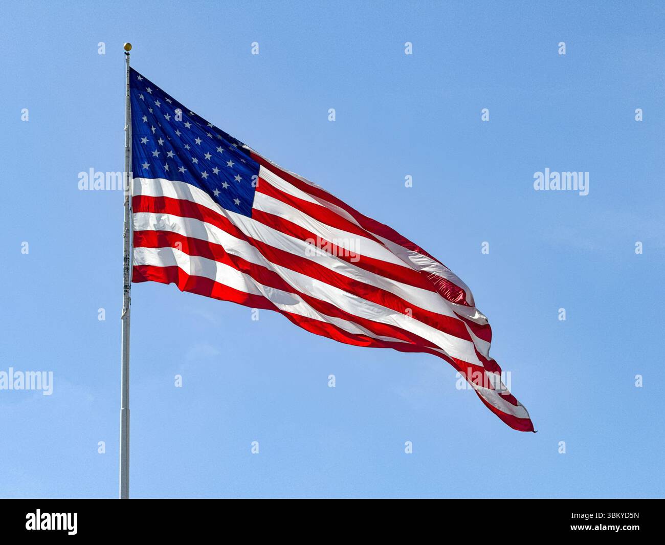 Large national flag of the United states of America, the Stars and Stripes, isolated against a clear blue sky. No people. - Smartphone Captured Stock Image