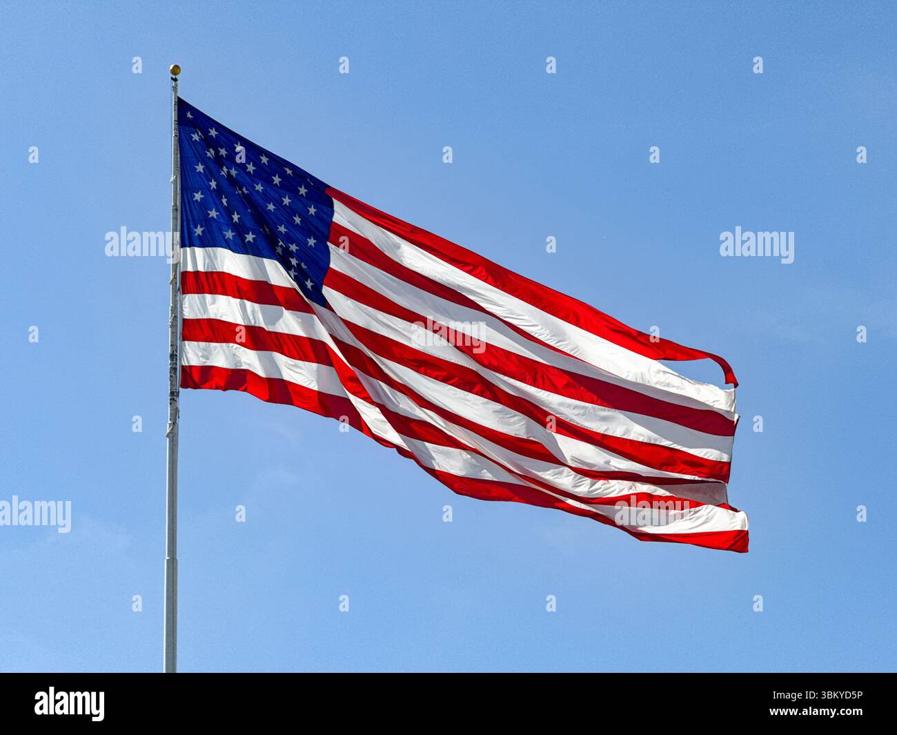 Large national flag of the United states of America, the Stars and Stripes, isolated against a clear blue sky. No people. - Smartphone Captured Stock Image