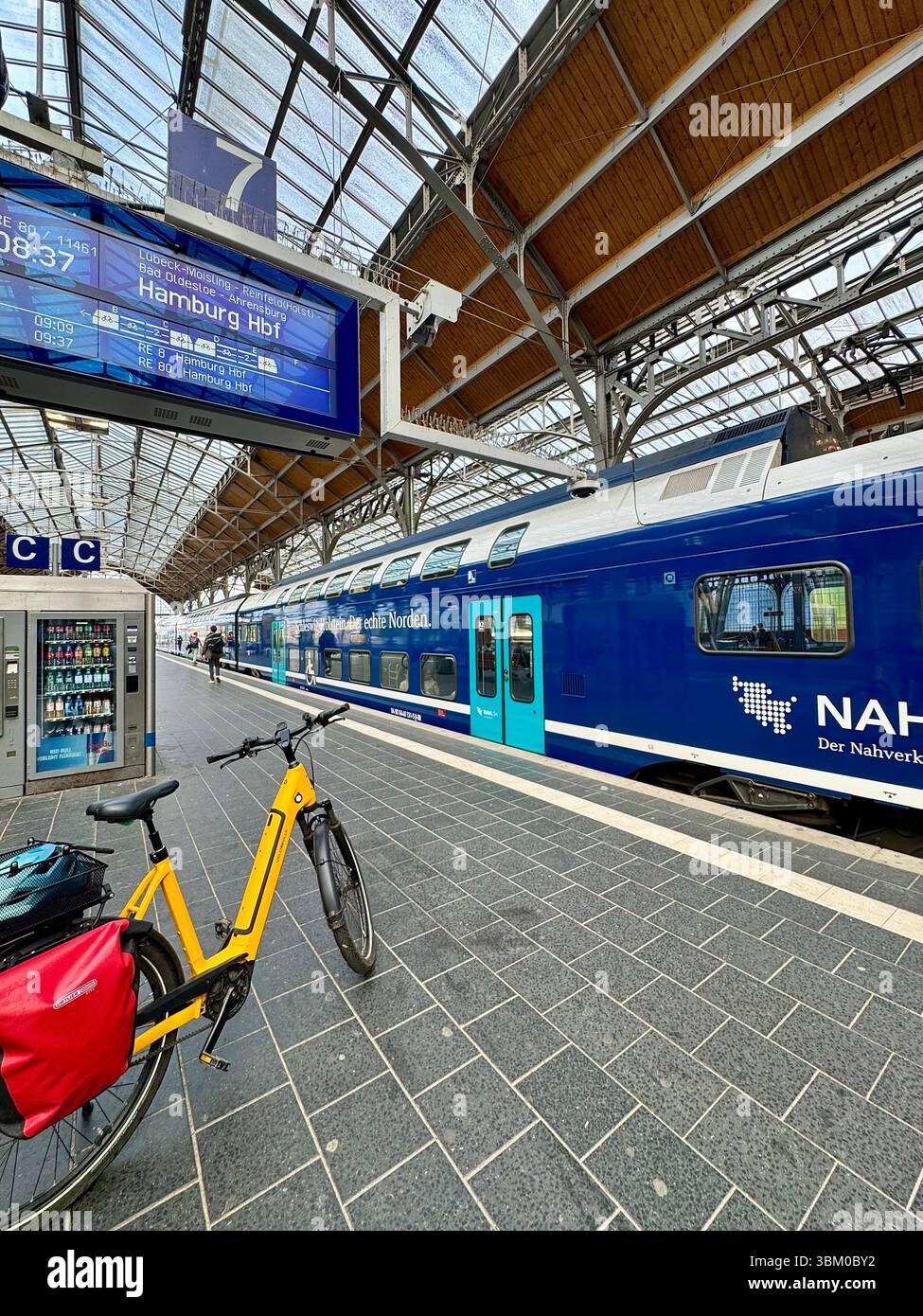Vibrant and modern scene at Lübeck train station in northern Germany. In the foreground, a bright yellow bicycle symbolizing eco-friendly travel - Smartphone Captured Stock Image