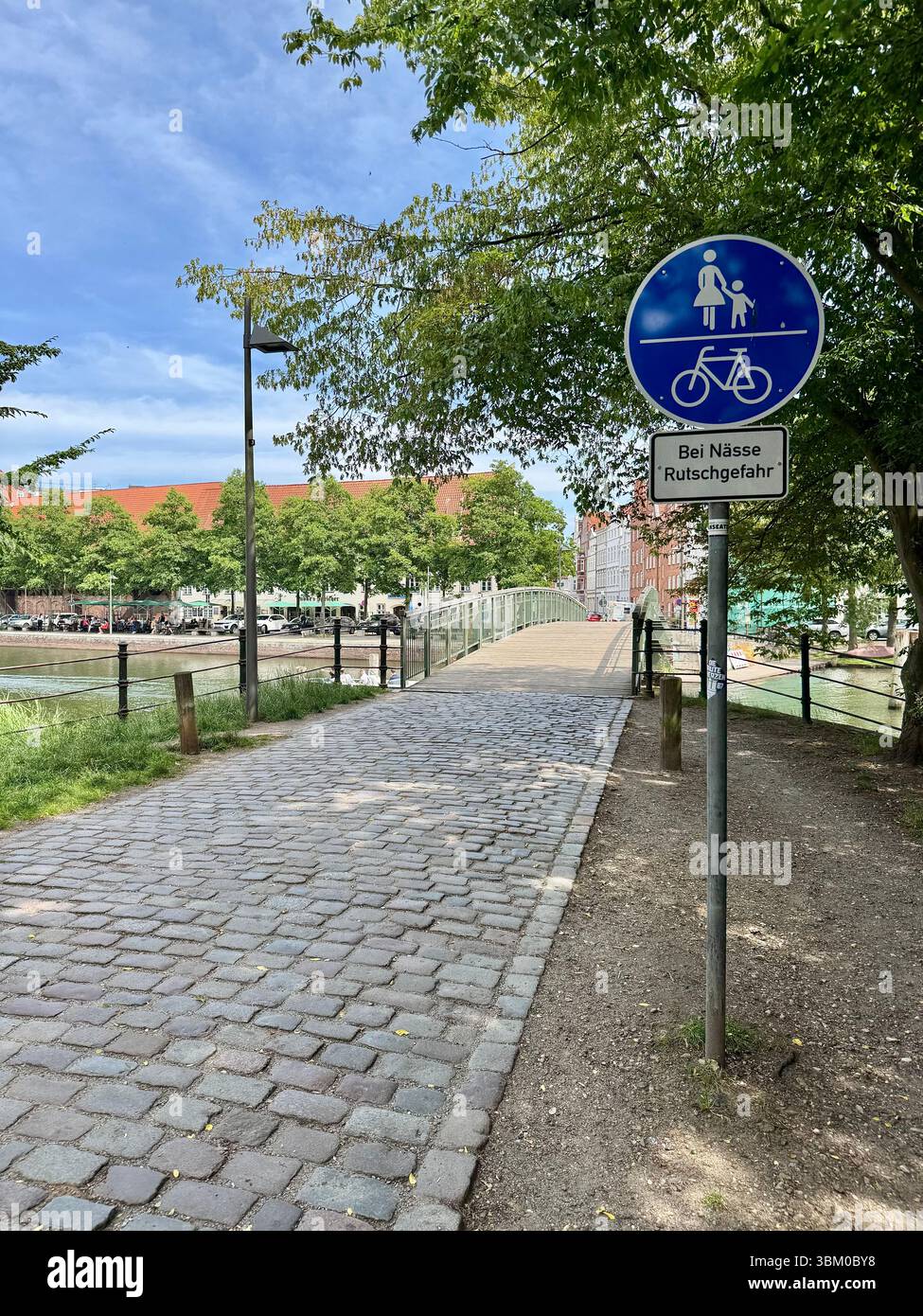 Shared pedestrian and bicycle path through a tree-lined cobblestone lane in  lubeck, Germany, with warning sign for slippery conditions. - Smartphone Captured Stock Image Shared pedestrian and bicycle path through a tree-lined cobblestone lane in  lubeck, Germany, with warning sign for slippery conditions. - Smartphone Captured Stock Image