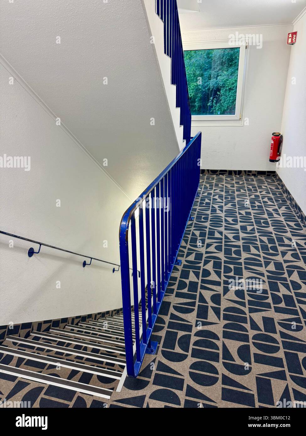 Interior view of a hotel stairwell with blue railing and patterned carpet in Lübeck, Germany. Stock Photo