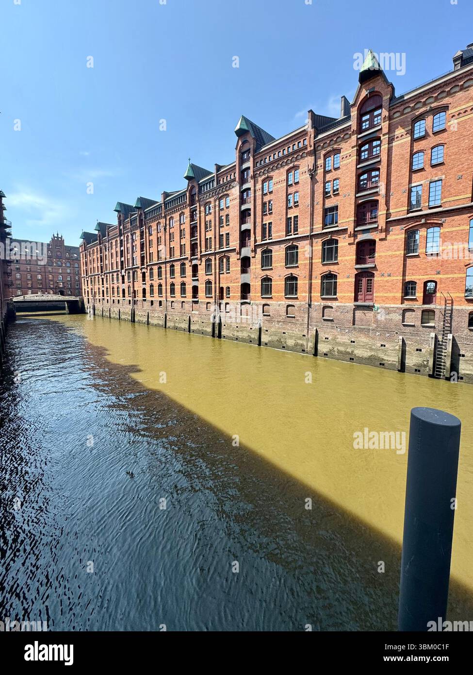 Red‑brick warehouse façades lining a sunlit canal in Hamburg’s Speicherstadt district, Germany. - Smartphone Captured Stock Image