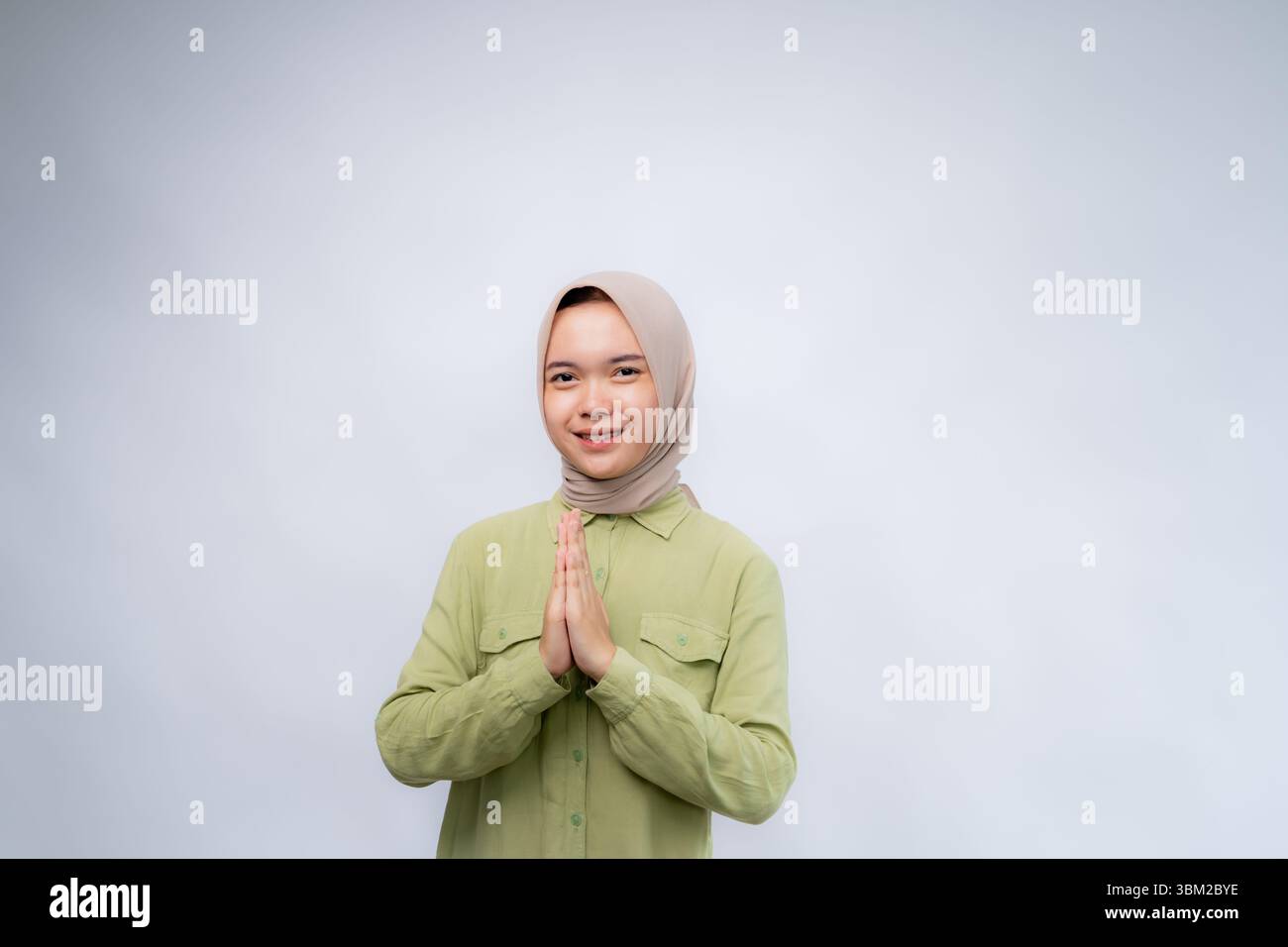 Smiling young Asian Muslim woman gesturing Eid Mubarak greeting isolated over white background Stock Photo