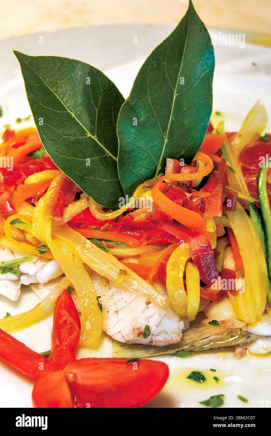 Close up of a delicious steamed fish fillet seasoned with saffron, accompanied by a colorful mix of vegetables, including carrots, zucchini, and peppe Stock Photo