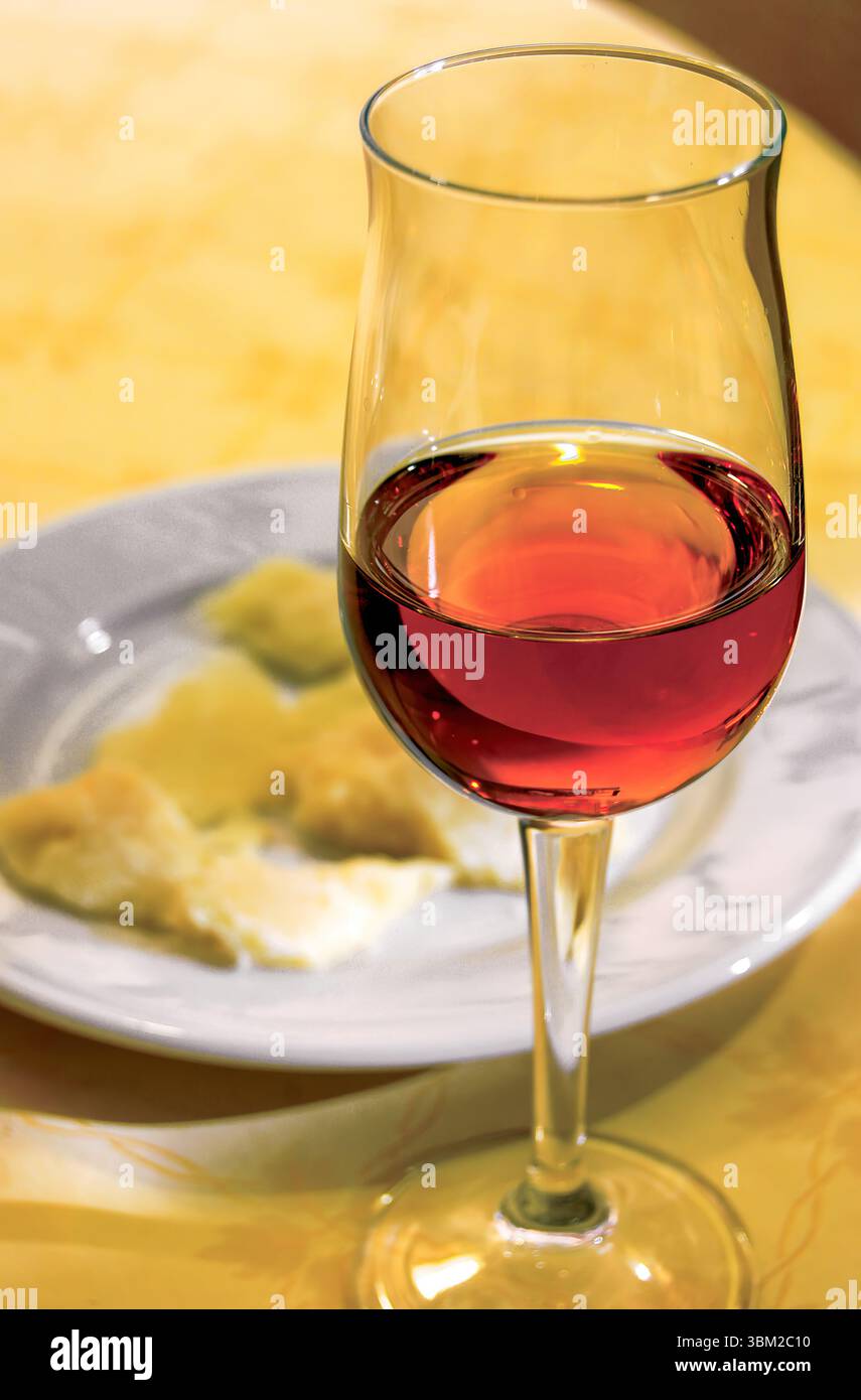 Glass of amber wine with cheese on a plate on yellow tablecloth, creating a sophisticated and inviting atmosphere for wine tasting and gourmet food pa Stock Photo
