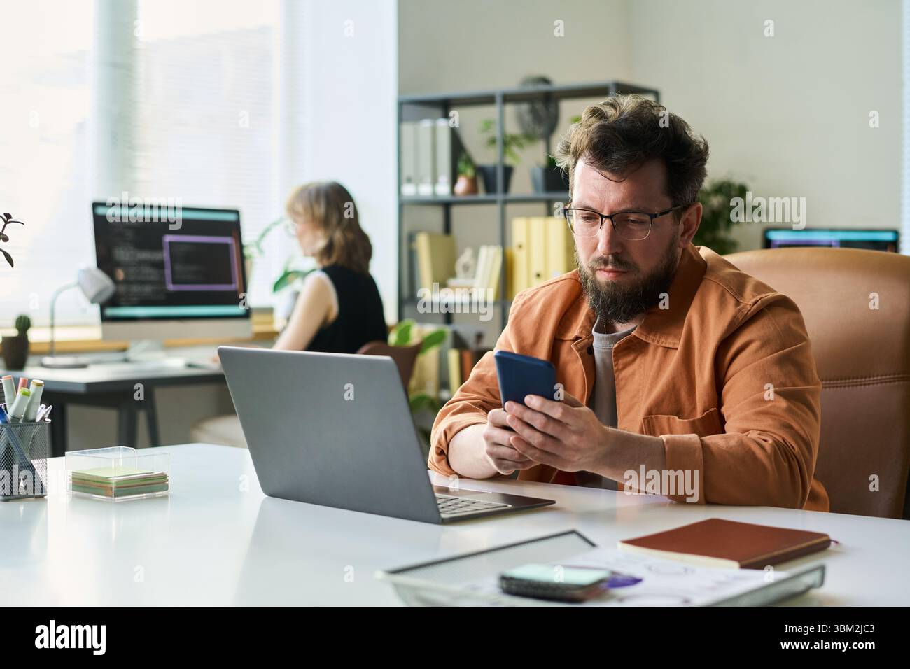 Caucasian Middle Aged Man Developing Neural Network Using Smartphone and Laptop Stock Photo