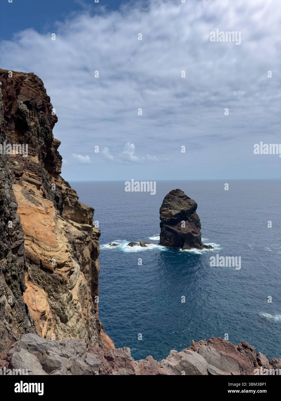 Ocean waves crash against towering rocky mountains on coast of Madeira, Portugal. Seascape features white surf, sea spray, and rugged rocks. - Smartphone Captured Stock Image
