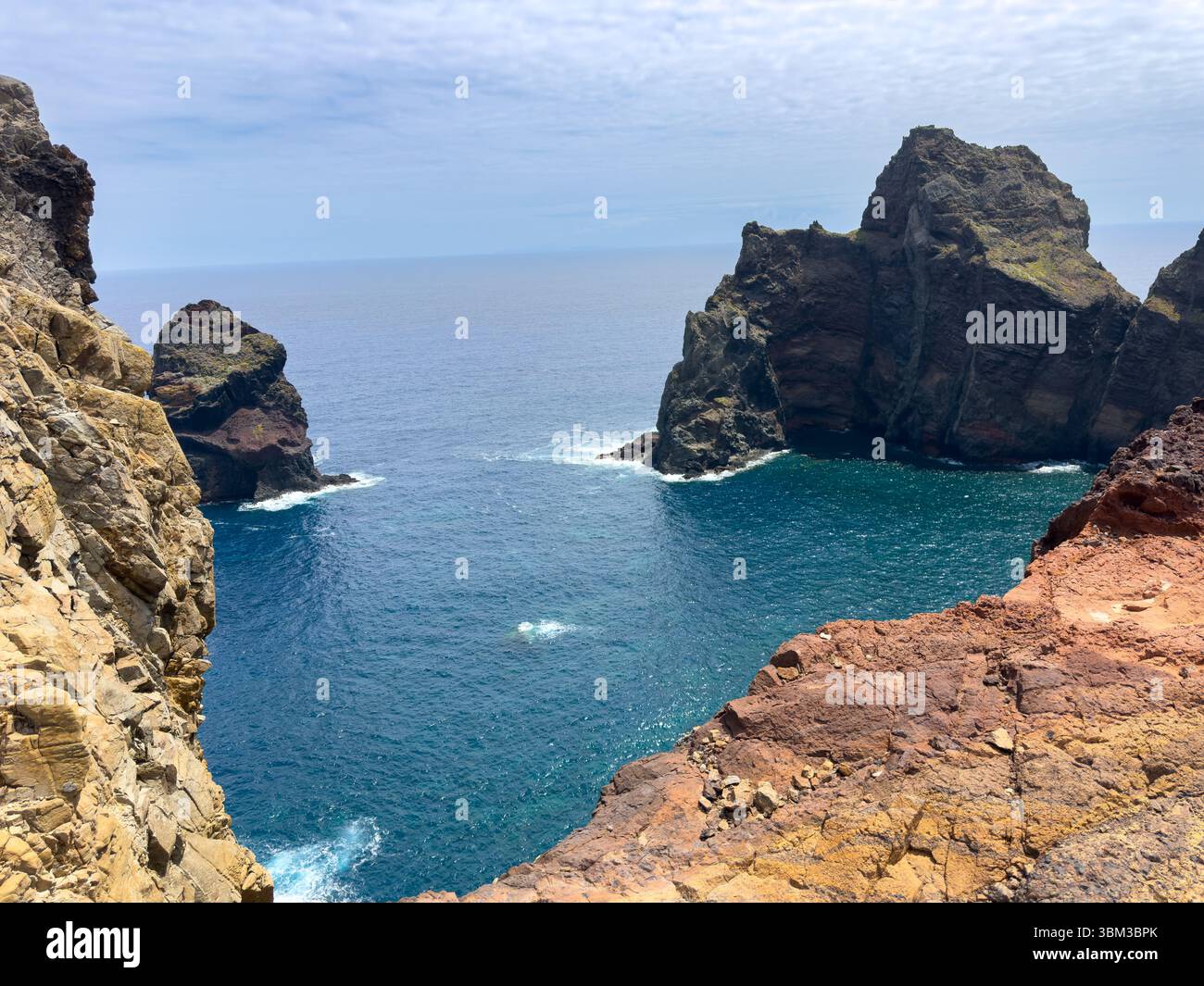 Madeira Island and a small bay with a high, rocky coastline. Ocean waves crash against large rocks, and mountains surround the area. Travel concept - Smartphone Captured Stock Image