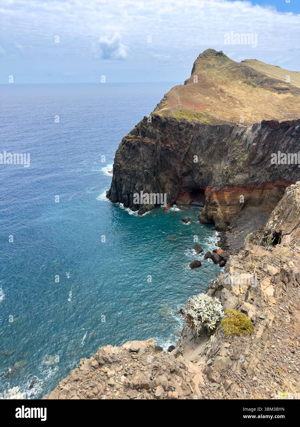 High cliffs on the shore of a small bay on the island of Madeira with a high rocky coastline, huge stones and ocean waves. Travel concept - Smartphone Captured Stock Image