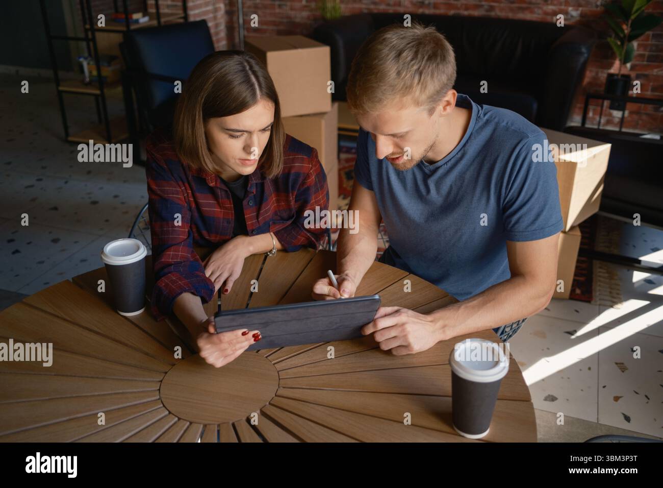 Two people collaborating on a tablet while sitting inside a modern workspace Stock Photo