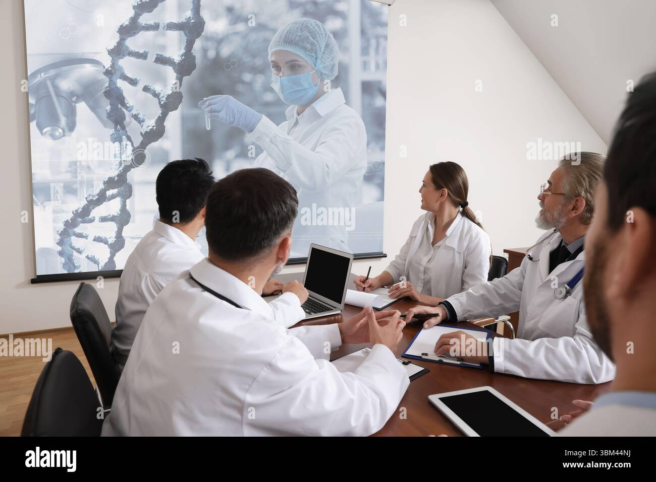 Team of doctors using video projector during conference about DNA indoors. Illustrations on projection screen Stock Photo