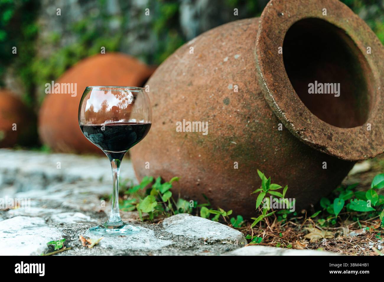 A glass of red wine stands beside traditional Georgian qvevri large ...