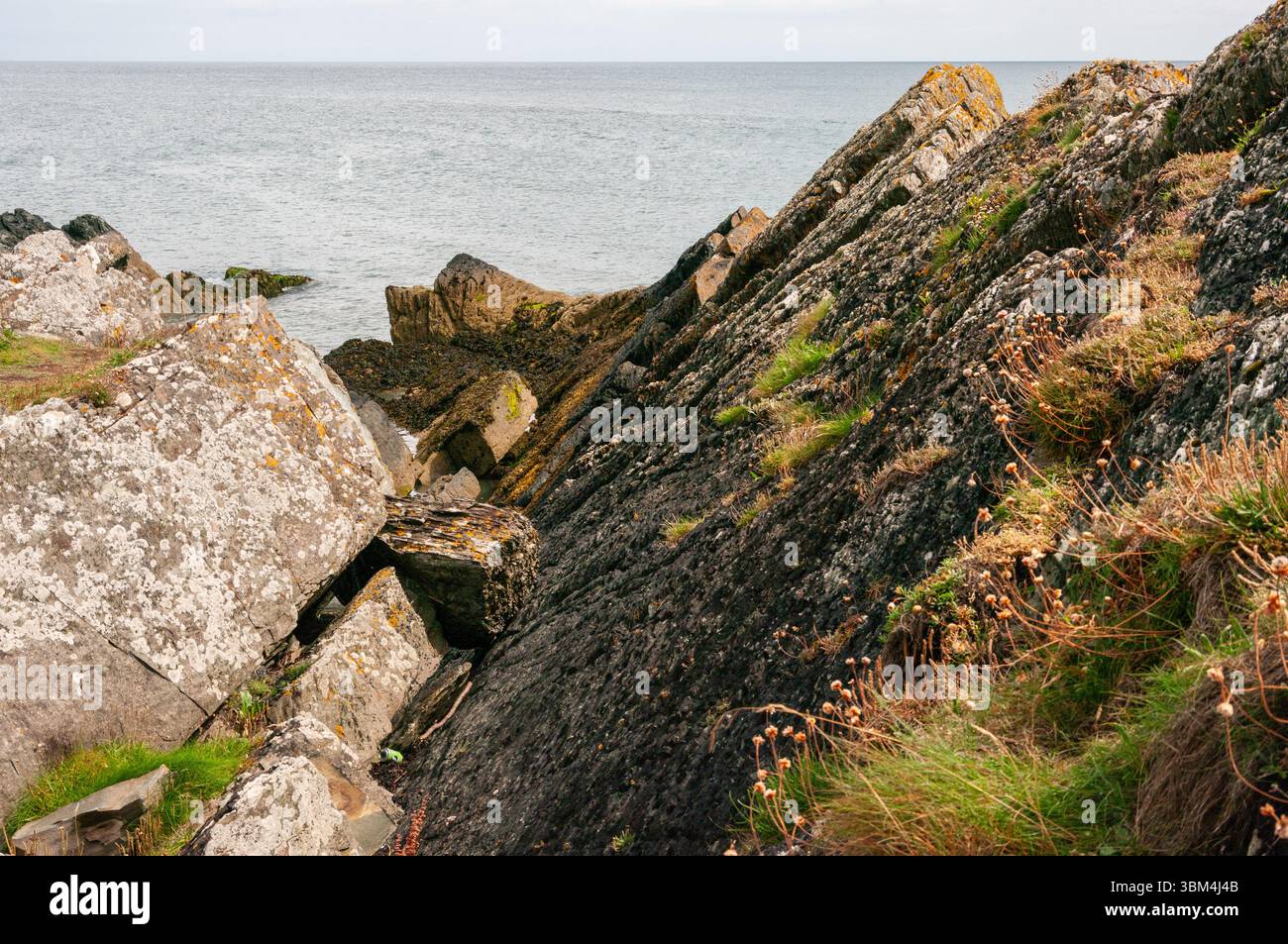 A rocky shoreline with a small body of water in the background. The ...