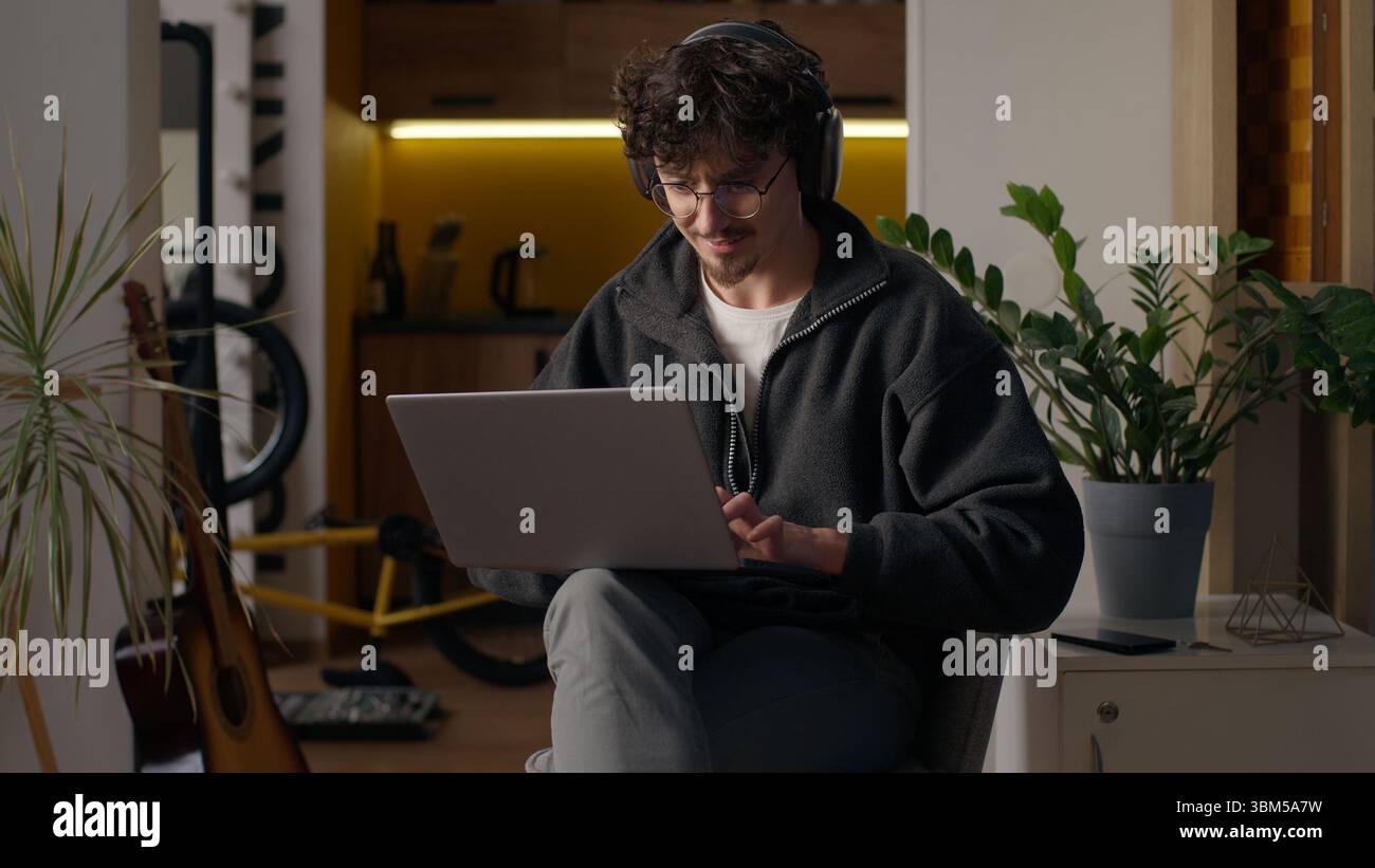 Glad Hispanic guy worker using laptop at home man freelancer typing computer programmer work remote job developer browse web male in headphones Stock Photo
