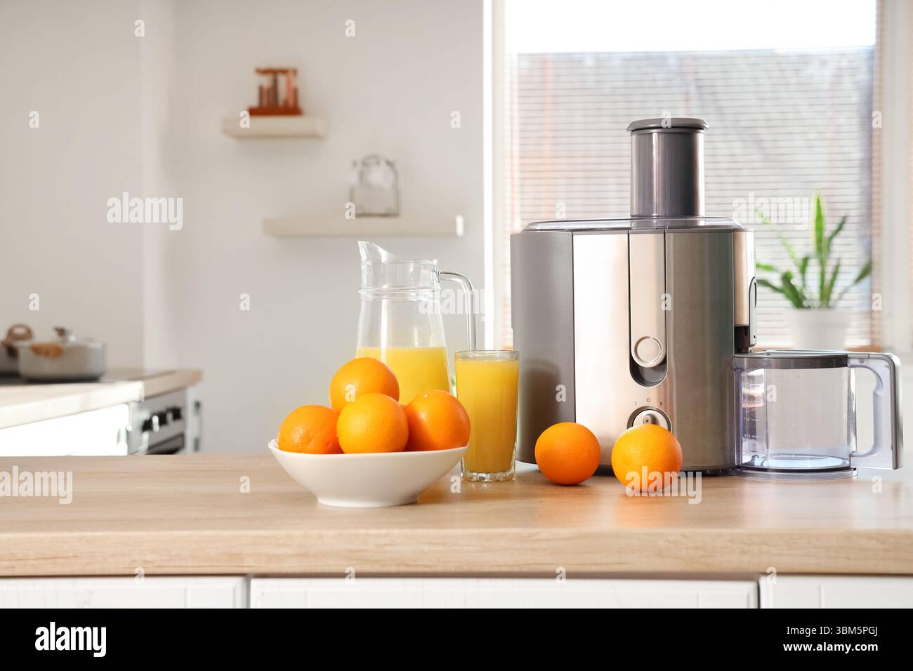 Modern juicer with oranges on table in kitchen Stock Photo
