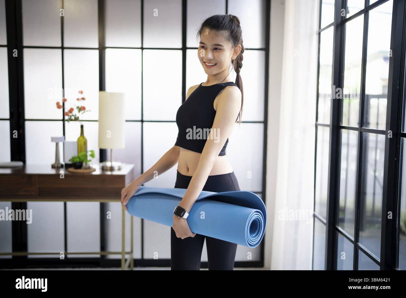 Fitness woman folding exercise mat before working out in yoga studio. rolling Yoga mat after training healthy lifestyle Stock Photo