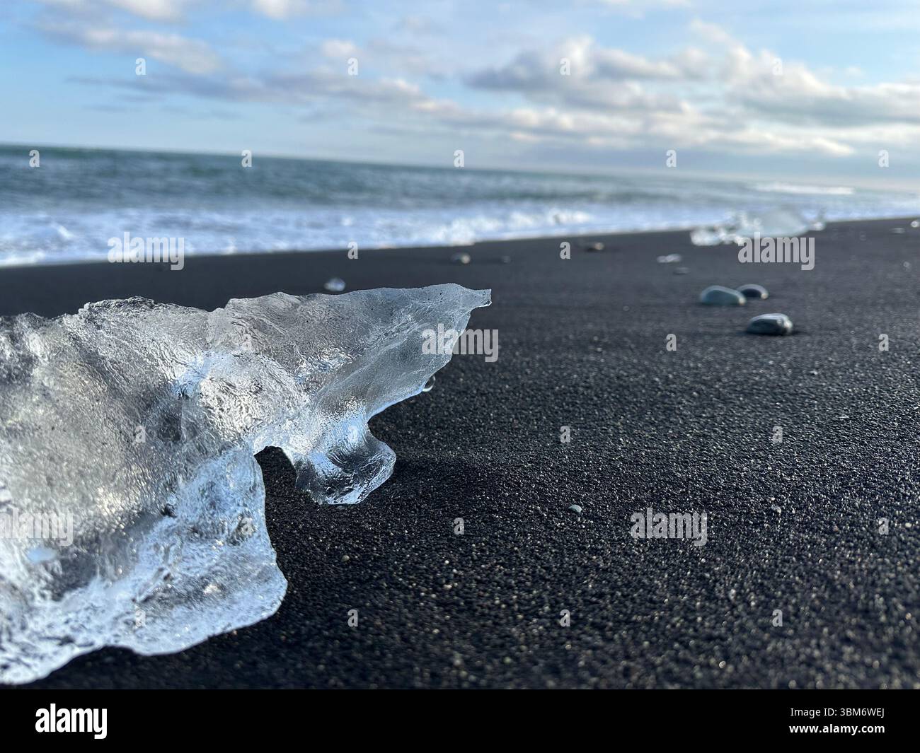 A close-up of a clear glacial ice fragment on the black volcanic sand ...