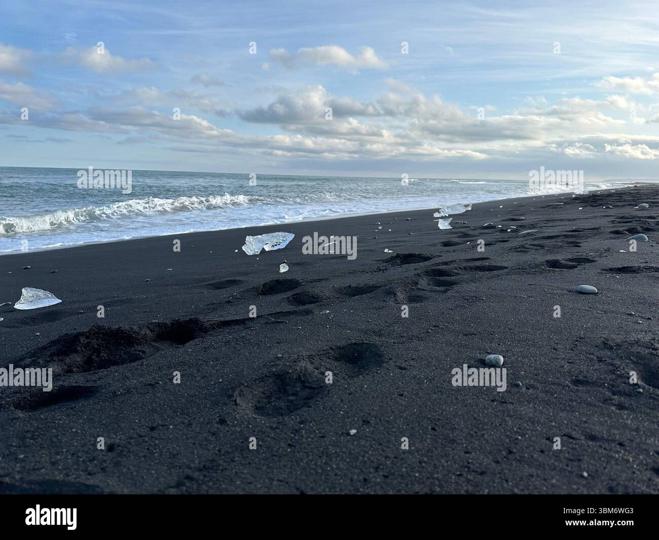 Icelandic landscape on Diamond beach south Iceland, small glacial ice chunks scatter a black sand beach with foot prints left in the sand - Smartphone Captured Stock Image