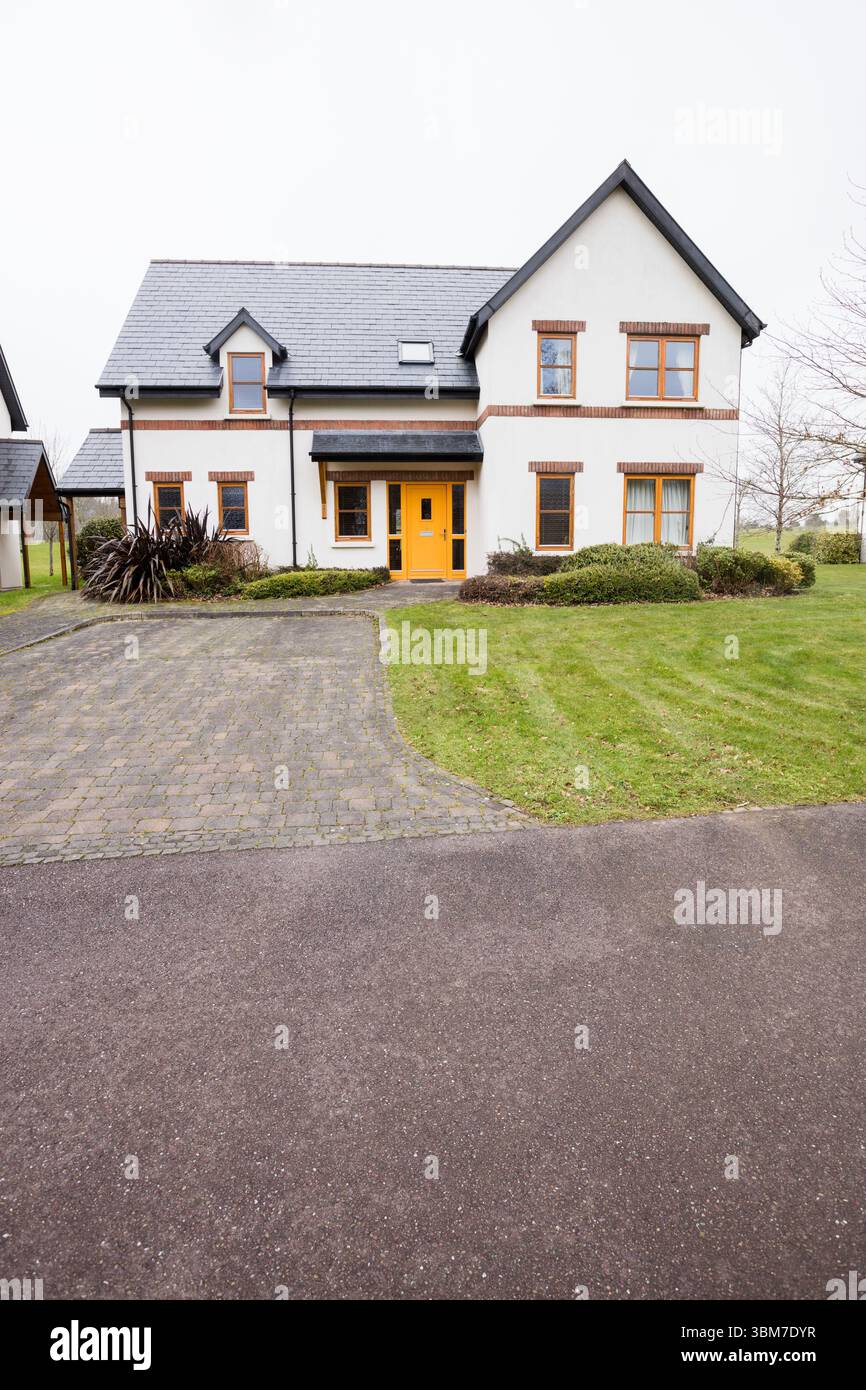 Flat design detached house sitting in yard, featuring steep gray roof, yellow door, driveway, lawn Stock Photo