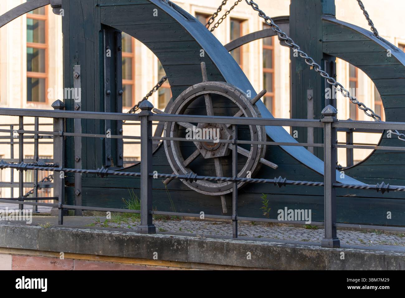 A wooden steering wheel is part of an old technical device with chains and metal rods. Historical craftsmanship meets functional design. Stock Photo
