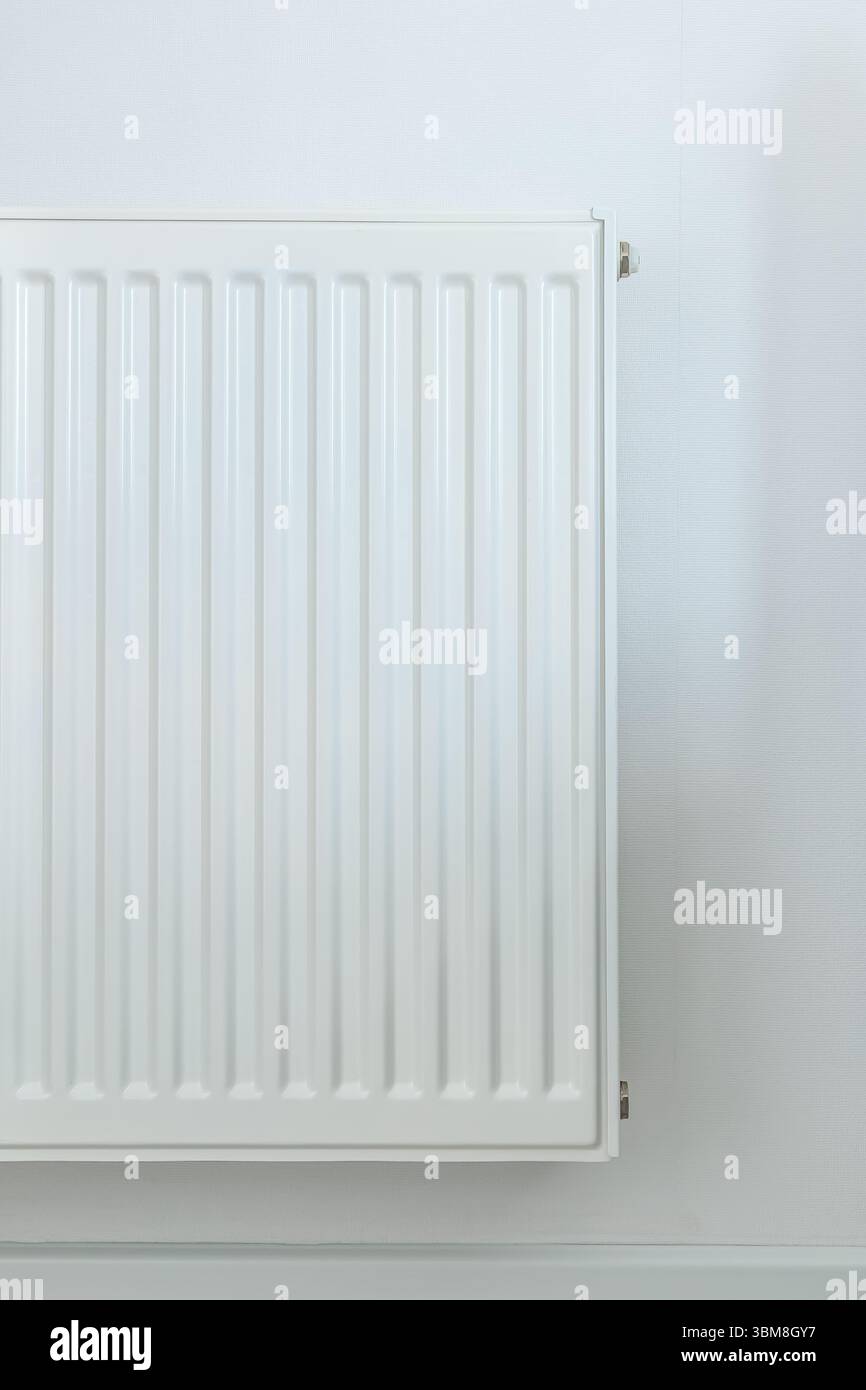 Partial view of a white radiator on a plain wall with subtle lighting ...