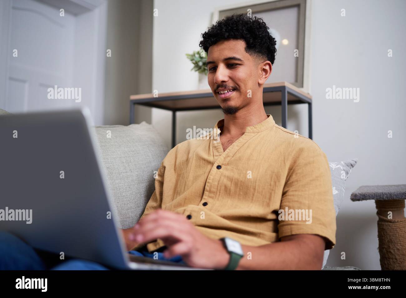 Young Man Smiling While Using a Laptop at Home in Relaxed Setting Stock Photo