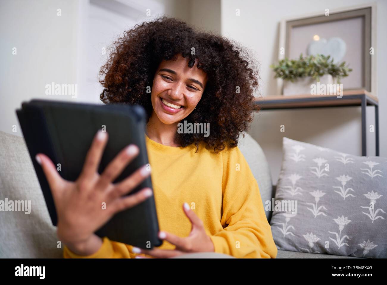 Young Woman Smiling While Using a Tablet in a Cozy Home Setting Stock Photo
