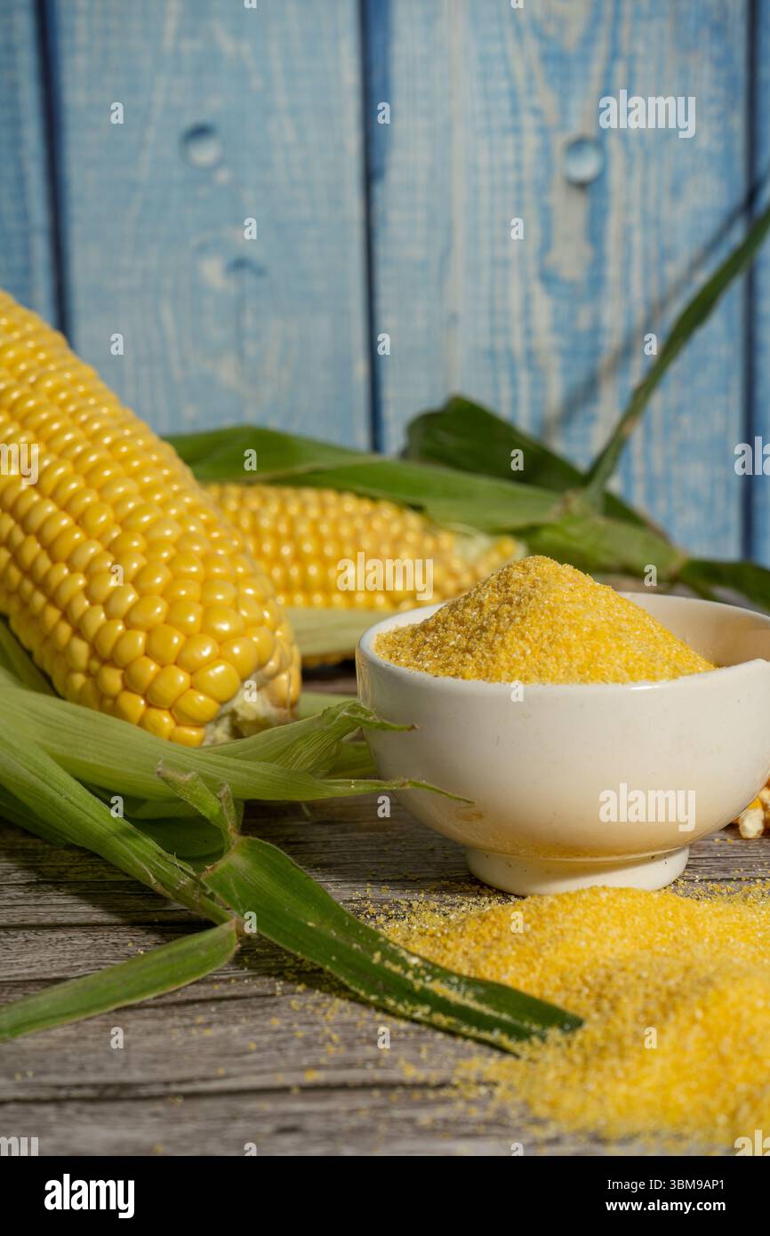 Corn flour in bowl with fresh corn cobs on rustic wooden table Stock Photo
