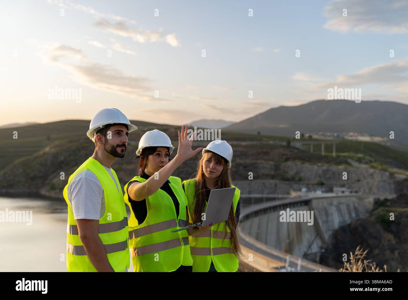 Engineers using laptop discussing project near dam at sunset Stock Photo