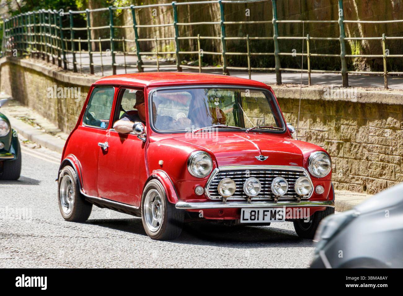Vintage red Mini Cooper driving on a city street with a stone wall and railing along the sidewalk. Stock Photo