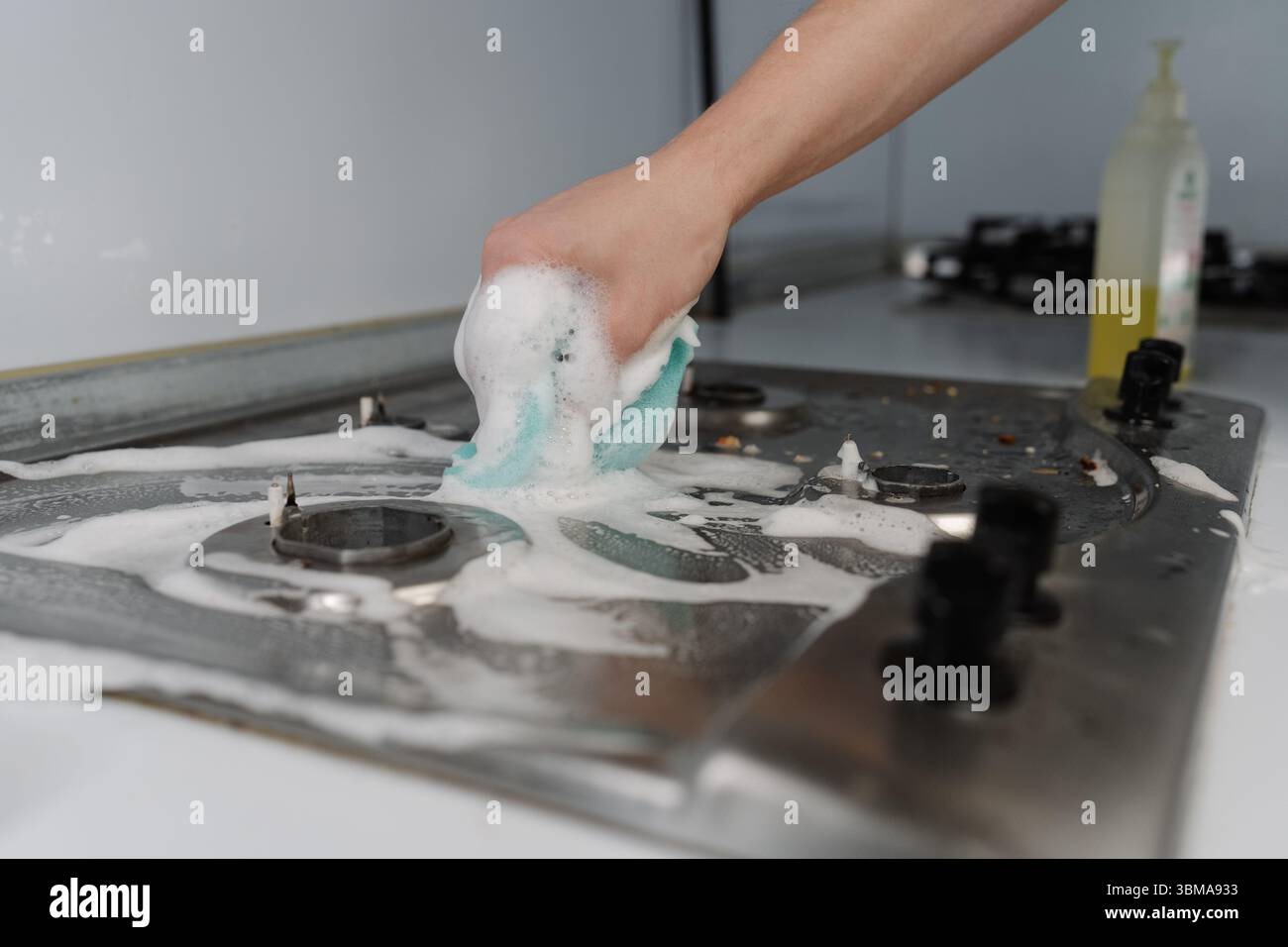 Male hand scrubbing gas stove with sponge and detergent, promoting ...