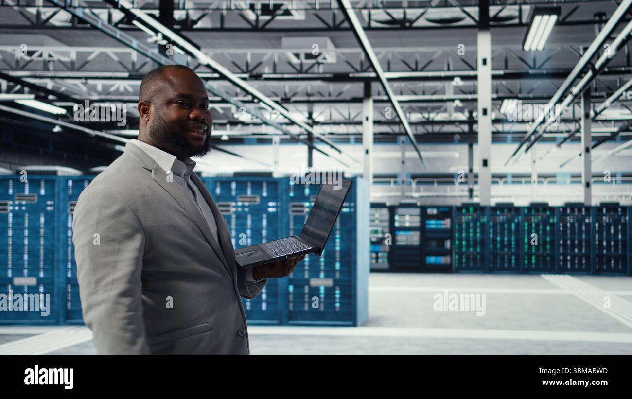 Data center engineer deploying AI driven management tools using laptop. Server farm employee inspecting server clusters, updating network topologies using artificial intelligence, camera A Stock Photo