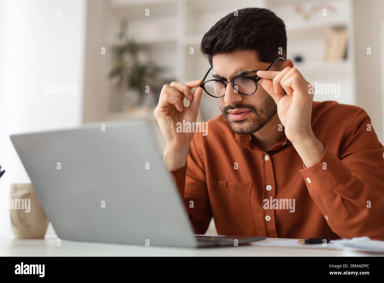Confused Arab guy using laptop looking at screen Stock Photo