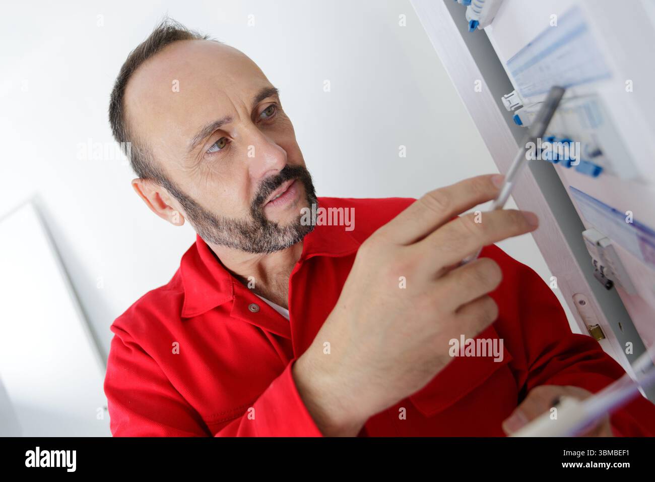 male technician holding clipboard while examining fusebox Stock Photo