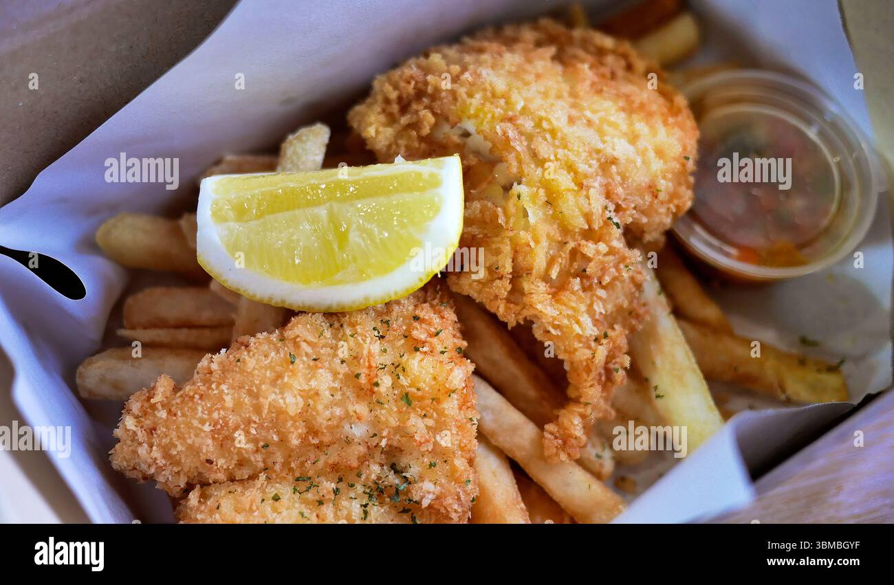 Classic Traditional English or British culinary delight Fish and Chips, golden deep fried fish with Lemon wedges in a paper box for takeaway as Lunch Stock Photo