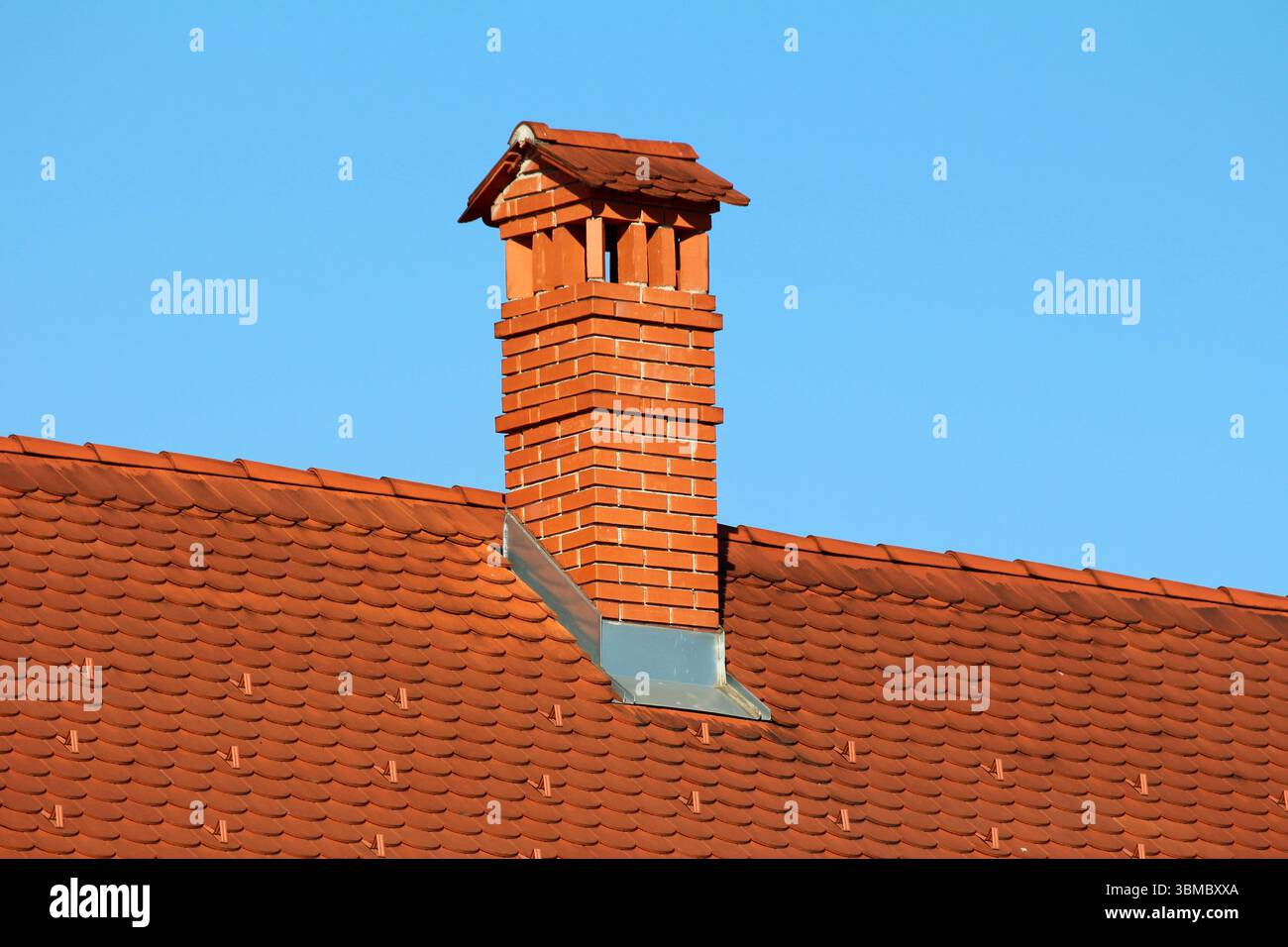 Tall red brick chimney with decorative cap rises from a red clay tile ...