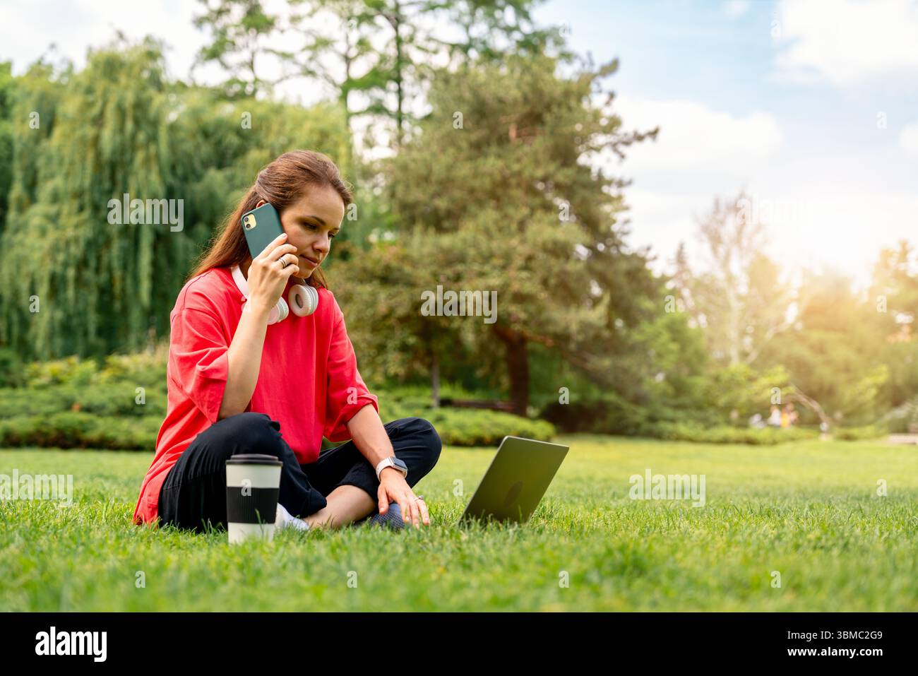 Young female freelancer using laptop and talking on phone outdoors Stock Photo