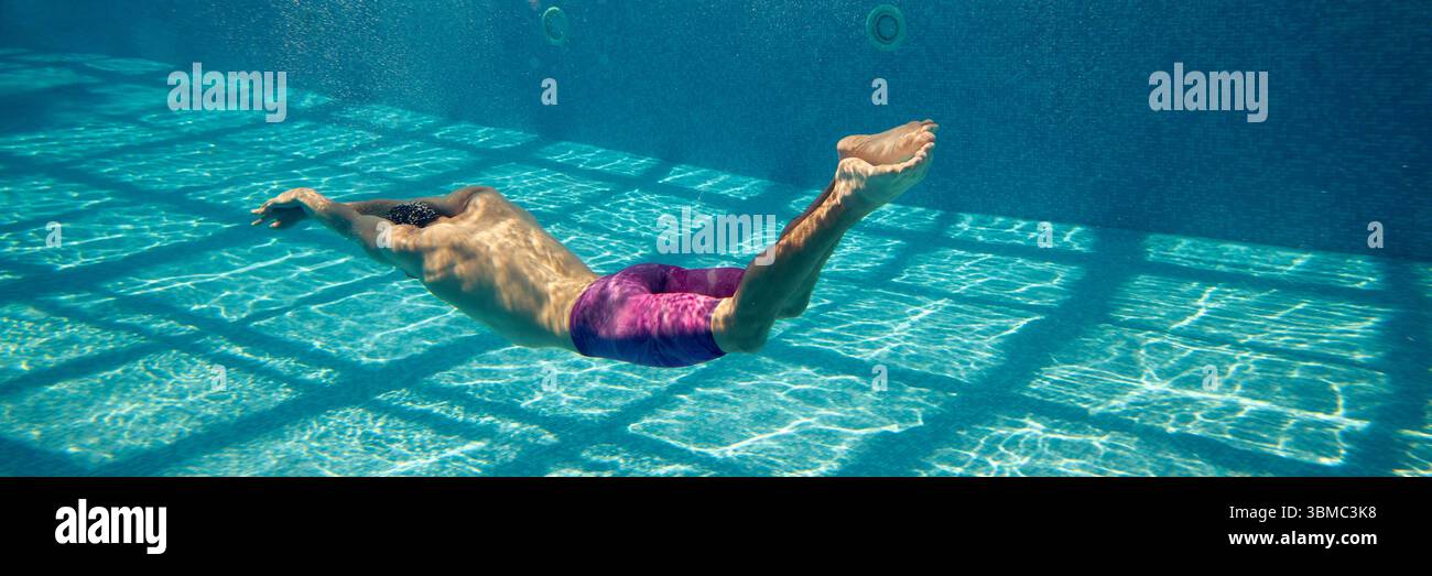 Person swimming underwater in pool with sunlight casting grid pattern ...