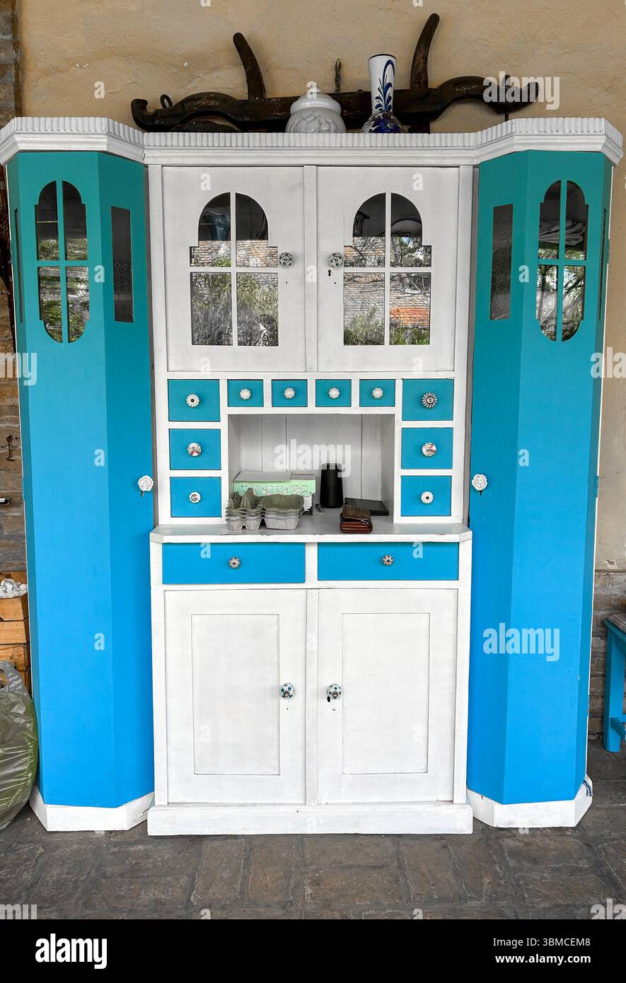 Old-fashioned blue and white kitchen cabinet with decorative drawers and glass-paneled doors, adding rustic charm to a cozy outdoor. - Smartphone Captured Stock Image