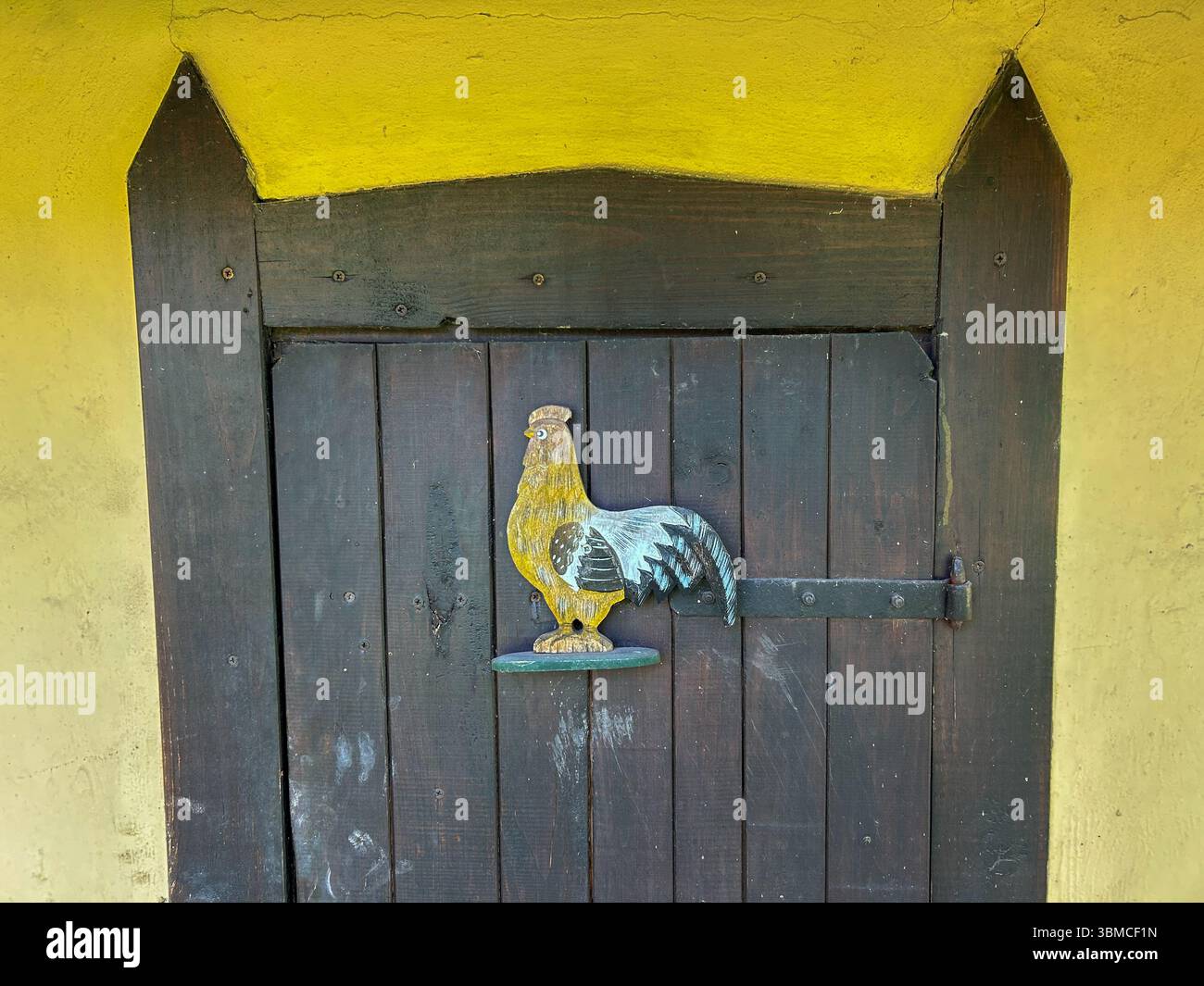 Close-up of a dark wooden door with a hand-painted rooster sign, set against a yellow wall, evoking a cozy rural or farmhouse atmosphere. - Smartphone Captured Stock Image