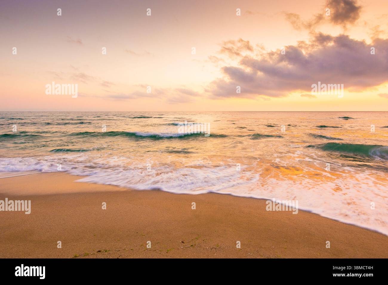 summer vacation at the sea. tranquil splash. beautiful purple pink seascape at sunrise. calm waves wash the golden sandy beach. fluffy clouds on the s Stock Photo