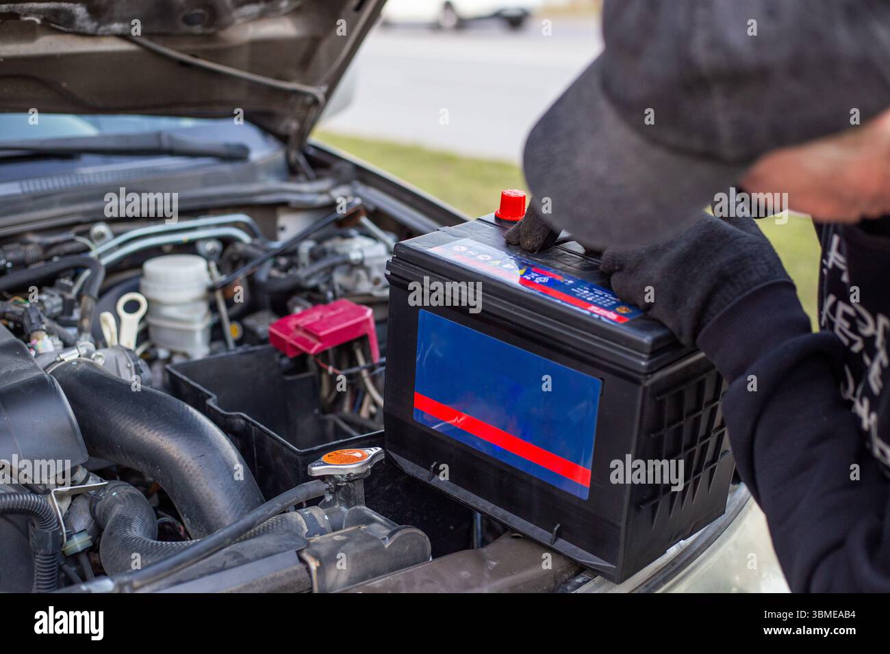 A man wearing gloves holds a battery pack over an engine bay, preparing to install it. Replacing a battery in a car. Stock Photo