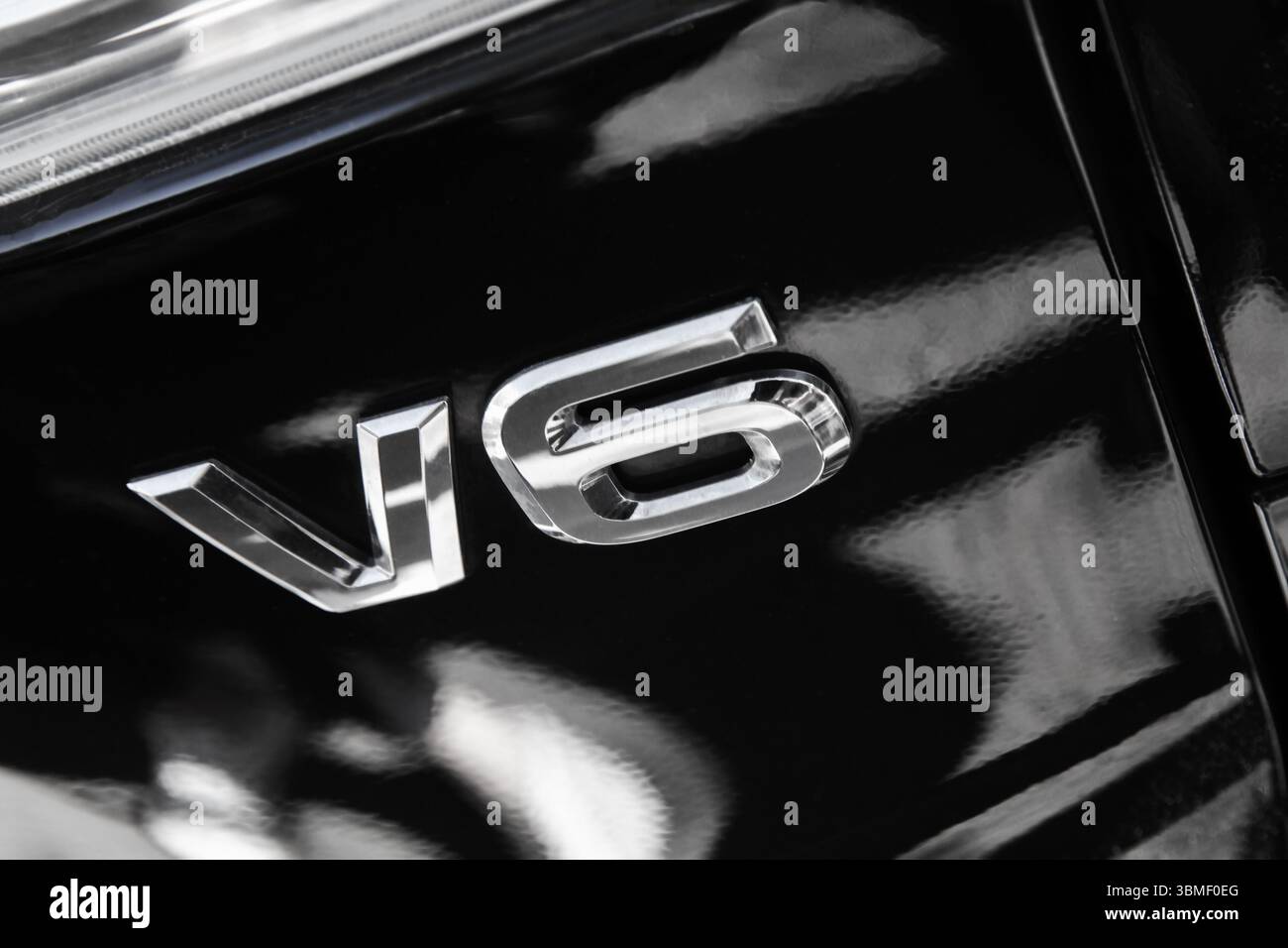 Detailed close-up showcasing the metallic V6 emblem on a sleek black exterior of an automobile with a reflective finish, highlighting power and style Stock Photo
