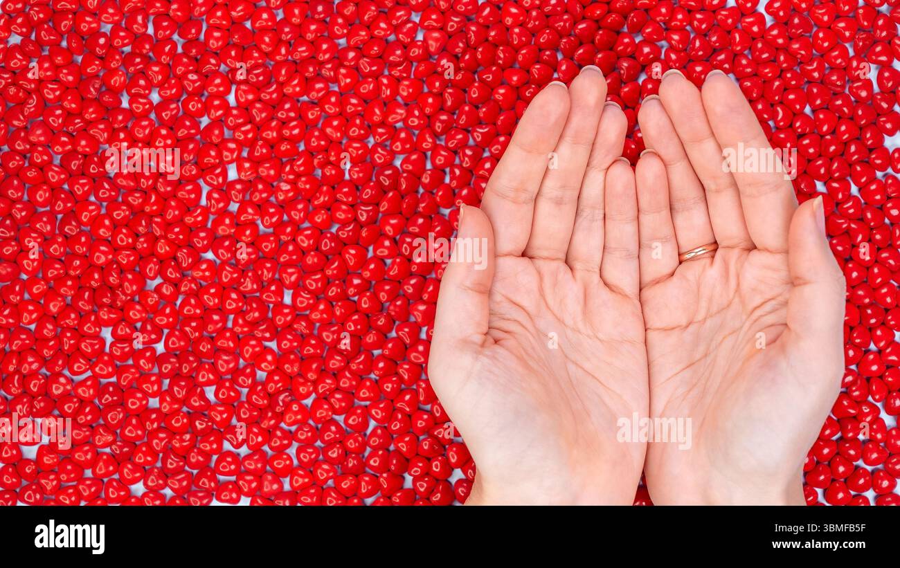 Female Hands holding together. Mockup design. A Pile of Heart Shaped Red Candies for Love and Romance on White Background. Stock Photo
