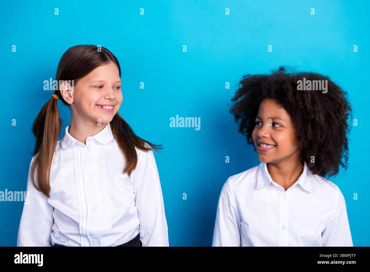 Two cheerful schoolgirls smiling brightly and facing each other ...