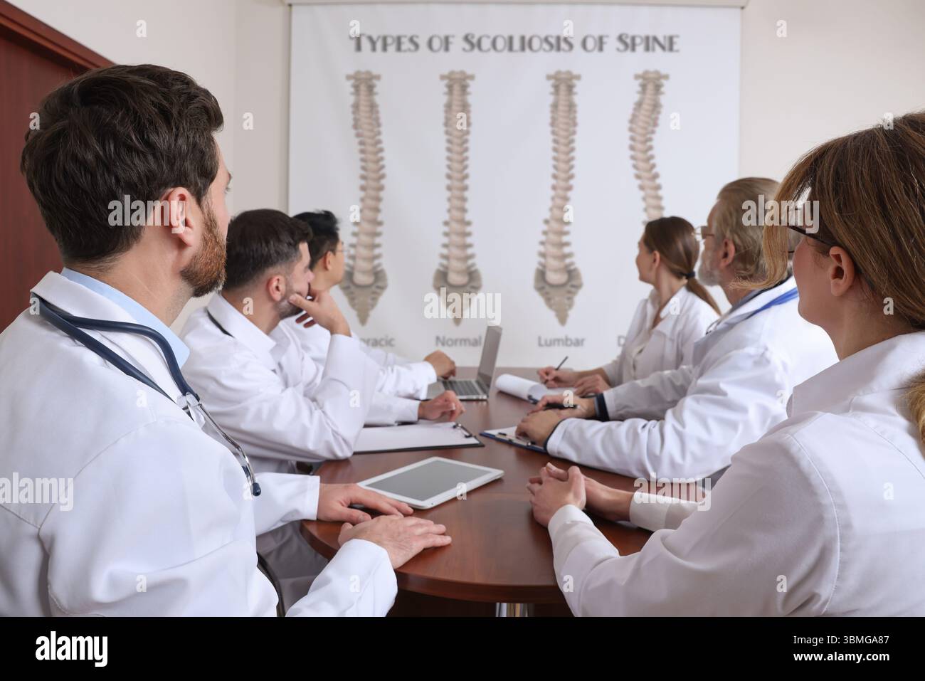 Team of doctors using video projector during conference about scoliosis indoors. Illustrations on projection screen Stock Photo