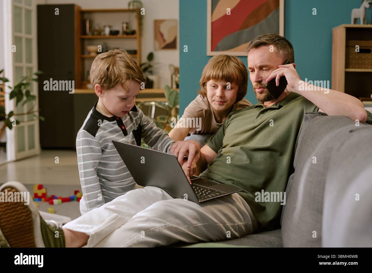 Middle Aged Man Working Remotely While Interacting with Children Stock Photo